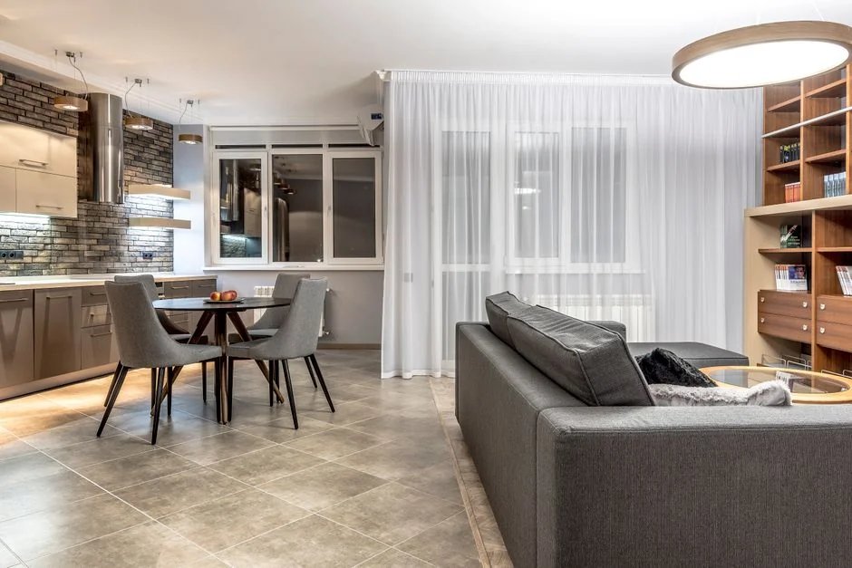 Covered with sheet sofa and floor lamp and packed cardboard boxes in light spacious room of new contemporary house